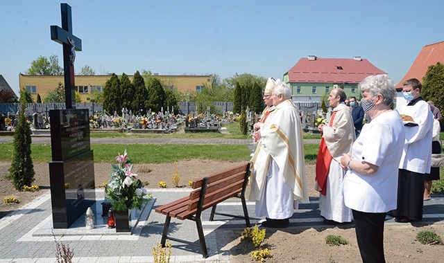 Modlitwa przy krzyżu na cmentarzu parafialnym. W tle budynki schroniska.