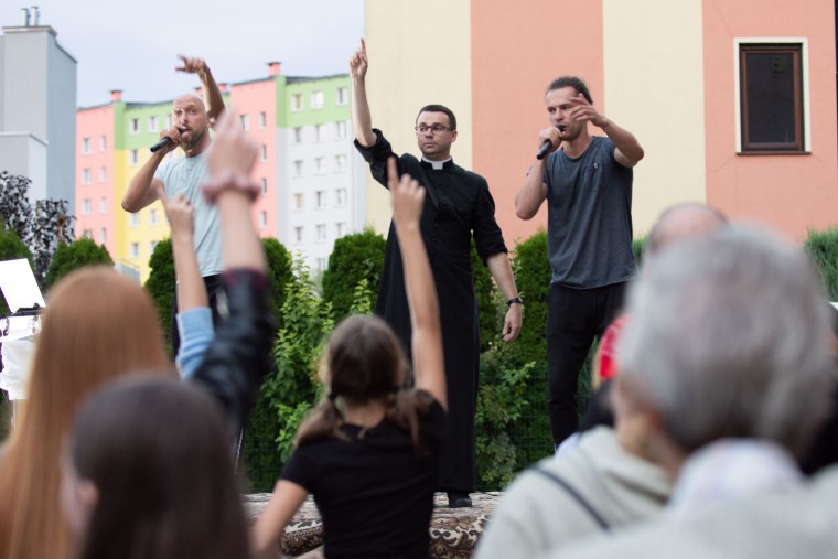 Ks. Dawid Fiołek na scenie z zespołem raperów.