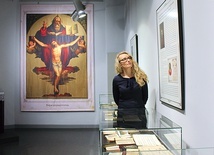 Anna Kulczyk. W tle wielkoformatowy wydruk z obrazem Trójcy Świętej pochodzącym z książki „Nauka wiary i obyczajów Kościoła katolickiego”.