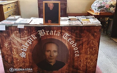 Stół z prasą katolicką i książkami wieńczy dibond z wizerunkiem zmarłego pijara.