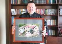 	Ksiądz Dariusz Tkaczyk pokazuje zdjęcie kościoła z czasu budowy.