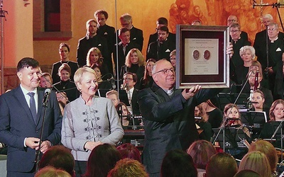 Ks. Fryderyk Tarabuła prezentuje medal Polonia Minor. Obok  –  Iwona Gibas i Rafał Kosowski.