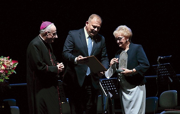 ▼	Bp Jacek Jezierski i Michał Missan, wiceprezydent Elbląga, wręczają Elżbiecie Szandrosze statuetkę i kwiaty.