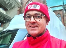 Ks. Daniel Marcinkiewicz w czerwonym stroju z logotypem Caritas.