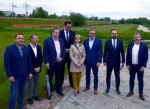 Uczestnicy konferencji na tle terenów w pobliżu linii kolejowej, na których zostanie zbudowana nowa nitka trasy z południa na północ Radomia.