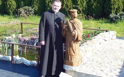 	Ks. proboszcz Rafał Wyleżoł przy rzeźbie patrona przy mostku jednej z alejek. 