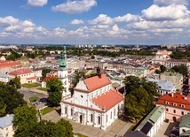 Zamość z lotu ptaka. Na pierwszym planie kolegiata. W tle skąpane w słońcu ulice przecinające się pod kątem prostym.