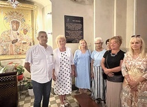Grupa dawnych uczniów na tle tablicy upamiętniającej nauczycielkę katechezy w oświęcimskim kościele Wniebowzięcia NMP.