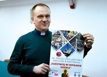 Ksiądz Krzysztof Bochniak prezentuje plakat promujący pielgrzymkę.