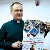 Ksiądz Krzysztof Bochniak prezentuje plakat promujący pielgrzymkę.