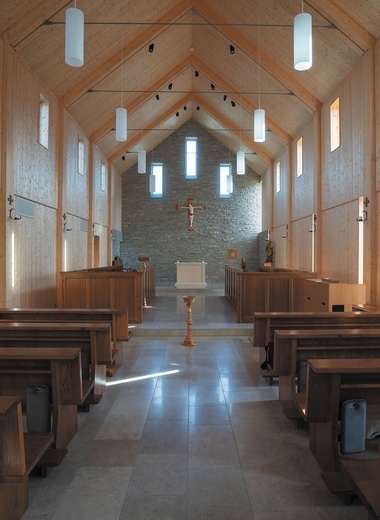 Minimalistyczne wnętrze prezbiterium przełamane kolorytem krucyfiksu.