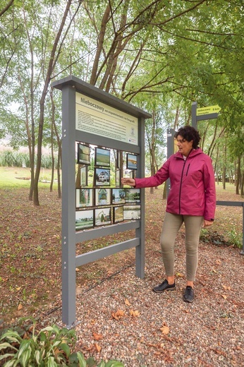 	Sołtys Barbara Mazurek przed tablicą ze zdjęciami „starych” Nieboczów – domami, gęsiami nad rzeką, łanami zbóż.