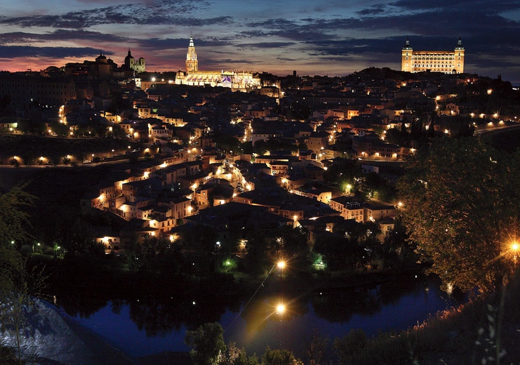 Panorama Toledo.  Ta dawna stolica  państwa Wizygotów  i późniejsza stolica Królestwa Hiszpanii została odzyskana  przez chrześcijan w 1085 roku. Dwa najbardziej oświetlone obiekty to gotycka katedra (w środku)  i alkazar (z prawej)  – dawna twierdza,  obecnie Muzeum Wojska.