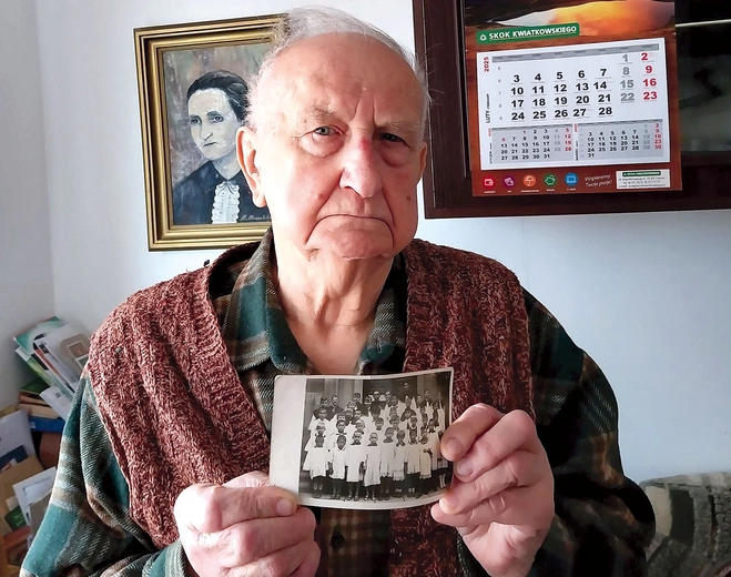 	Stanisław Talaga ze zdjęciem grupy ministranckiej z 1945 roku. Za nim na ścianie wisi portret jego mamy Magdaleny,  która spowiadała się u sługi Bożego.