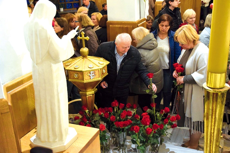 Wierni składają róże przed figurą świętej.