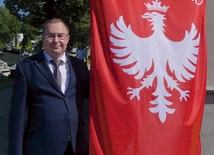 Archiwista żywieckiego cmentarza Przemienienia Pańskiego przy fladze powstańców śląskich. 